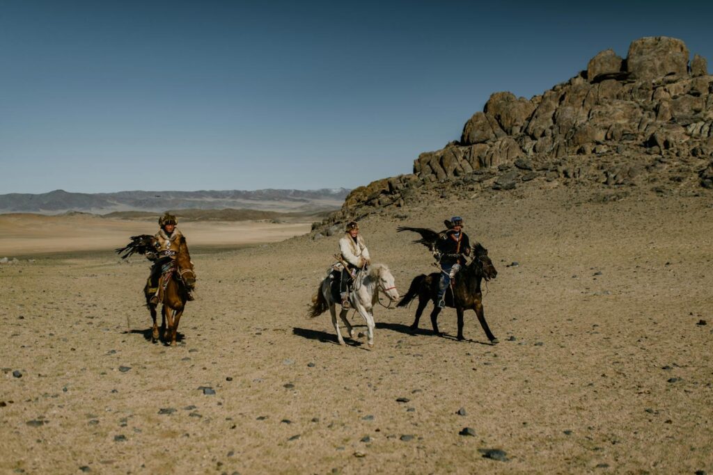 Three nomadic horse riders with eagles in a vast arid desert setting