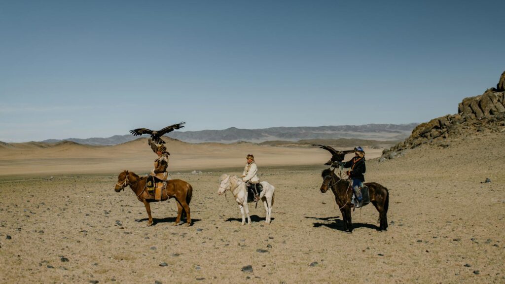 Traditional Mongolian eagle hunters on horseback in the vast desert landscape.