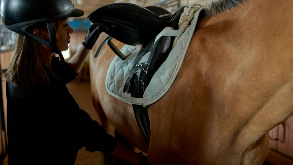 A female equestrian preparing her horse for riding in a stable setting.