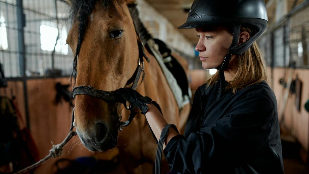 A woman in riding gear bonding with her horse inside a stable.