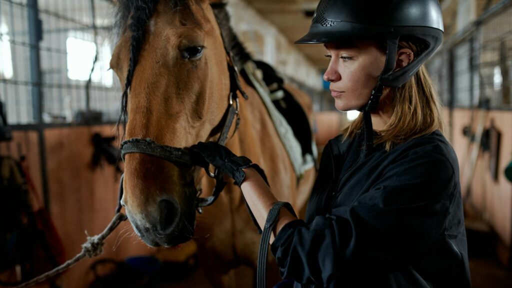 A woman in riding gear bonding with her horse inside a stable.