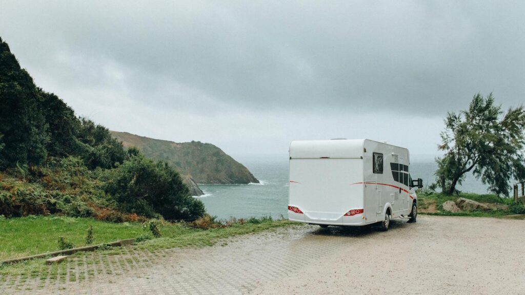 Serene coastal view with a caravan parked near the seaside under a cloudy sky.