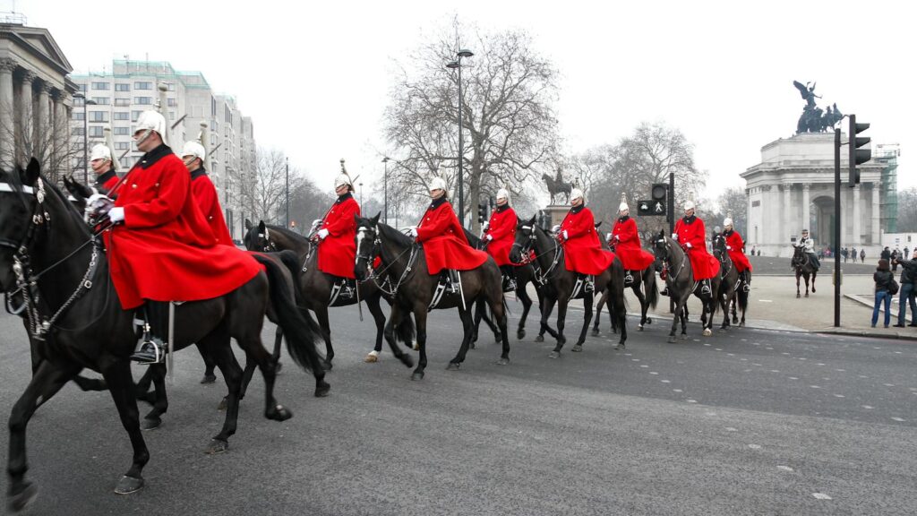 Horse Guards in red uniforms riding through London during a ceremonial parade.