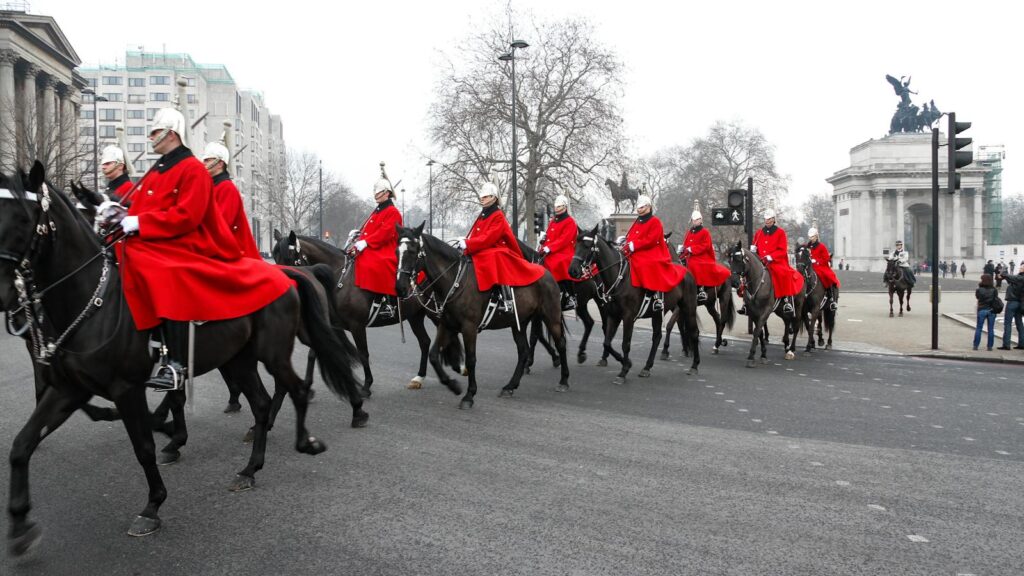 Horse Guards in red uniforms riding through London during a ceremonial parade.