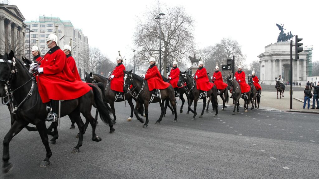 Horse Guards in red uniforms riding through London during a ceremonial parade.