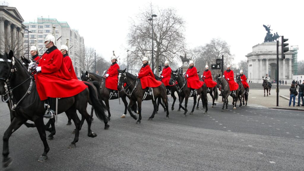 Horse Guards in red uniforms riding through London during a ceremonial parade.