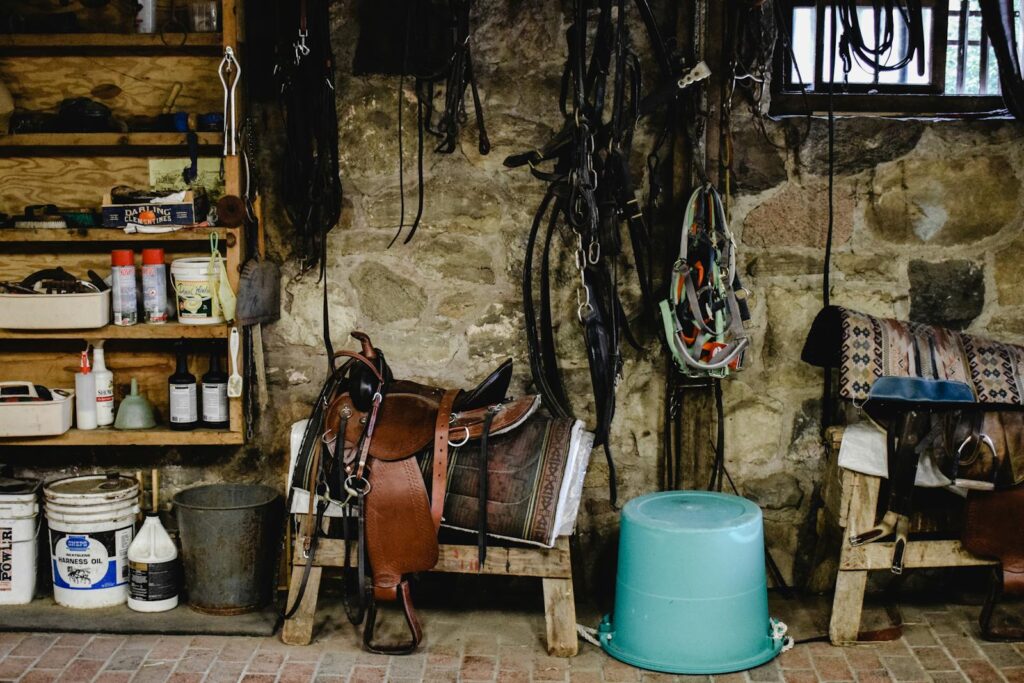 A cozy stable with equestrian equipment, including saddles and pails, against a stone wall.