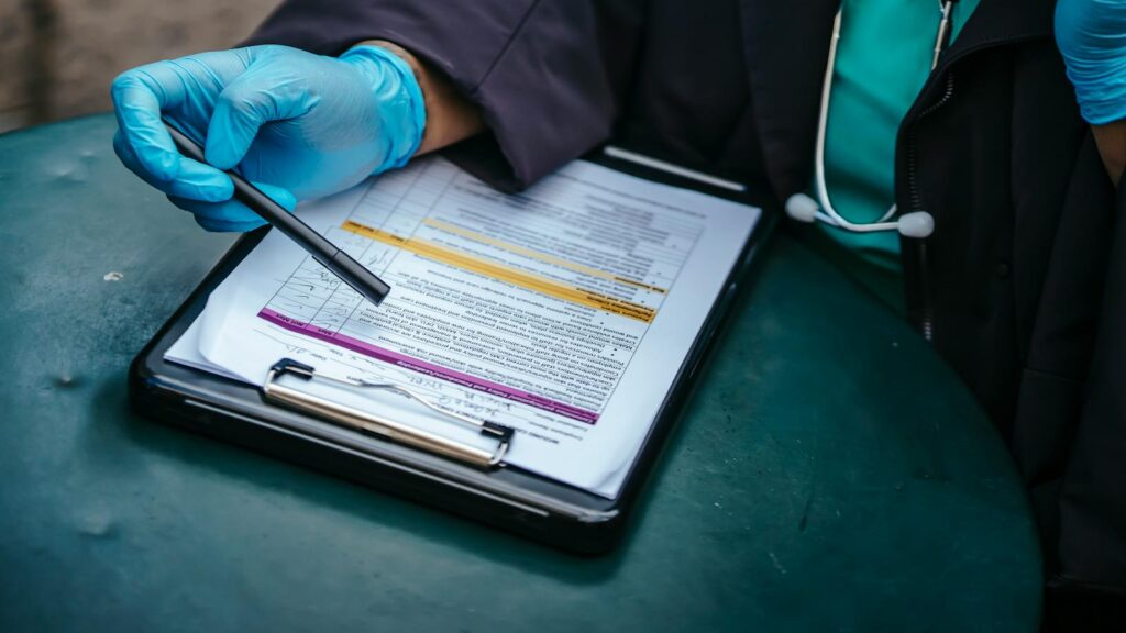 From above of crop anonymous plump female doctor in disposable gloves working at table with paper on clipboard