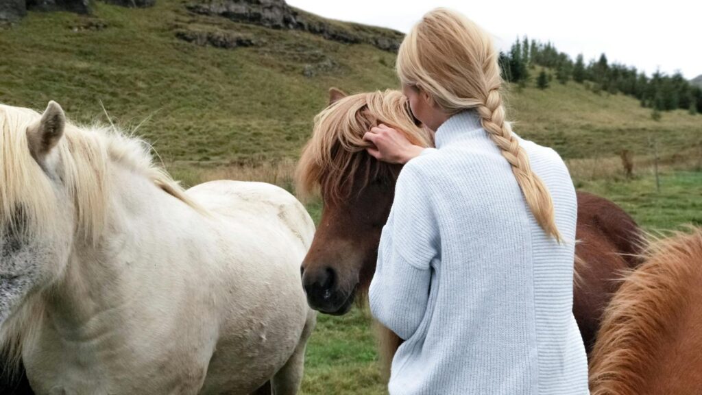 A woman with braids lovingly caresses horses in a lush rural meadow.