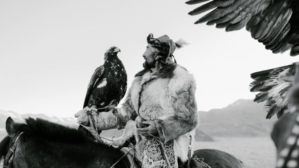 a Kazakh man in traditional attire with his eagle in a vast landscape.