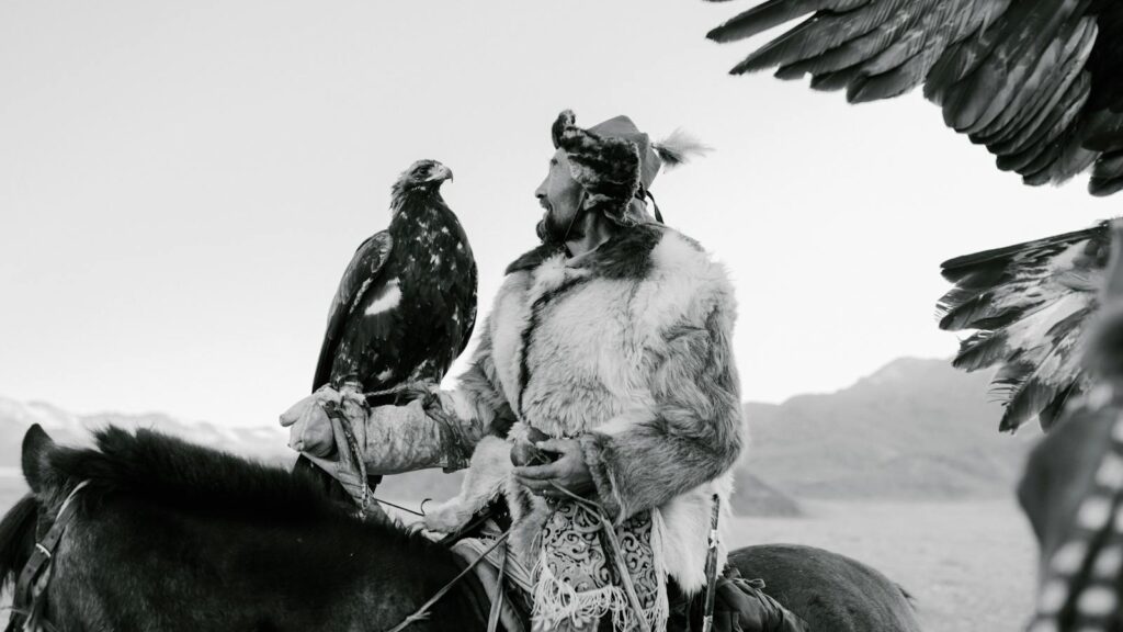 Capture of a Kazakh man in traditional attire with his eagle in a vast landscape.
