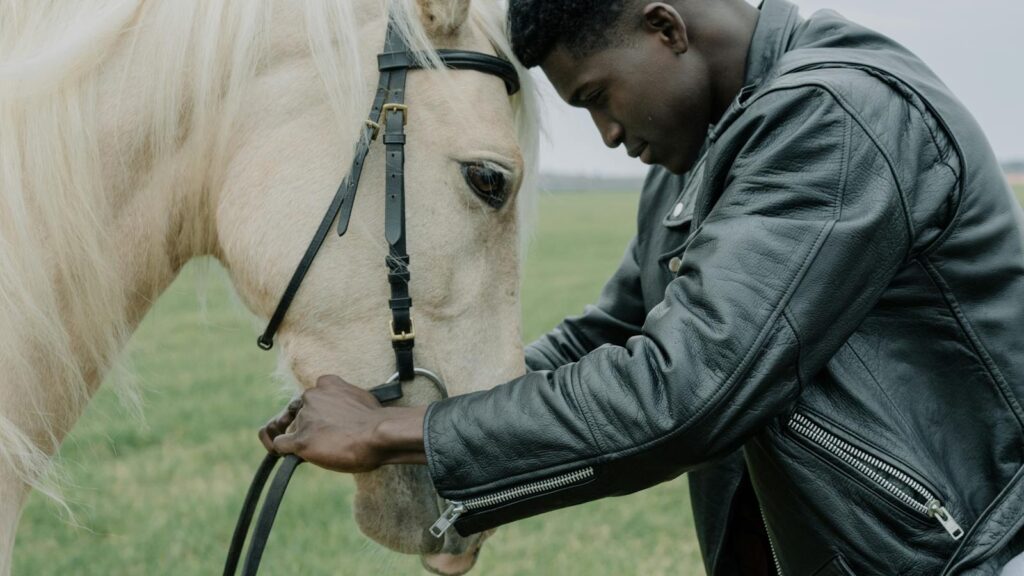 African American man gently interacting with a white horse outdoors.