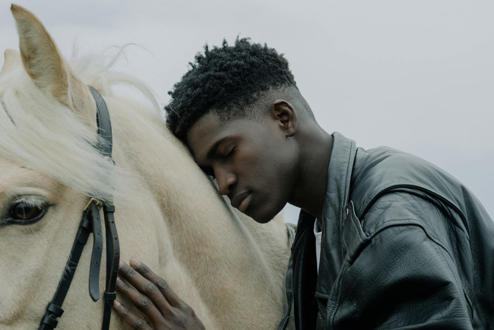Young man rests his head affectionately on a white horse