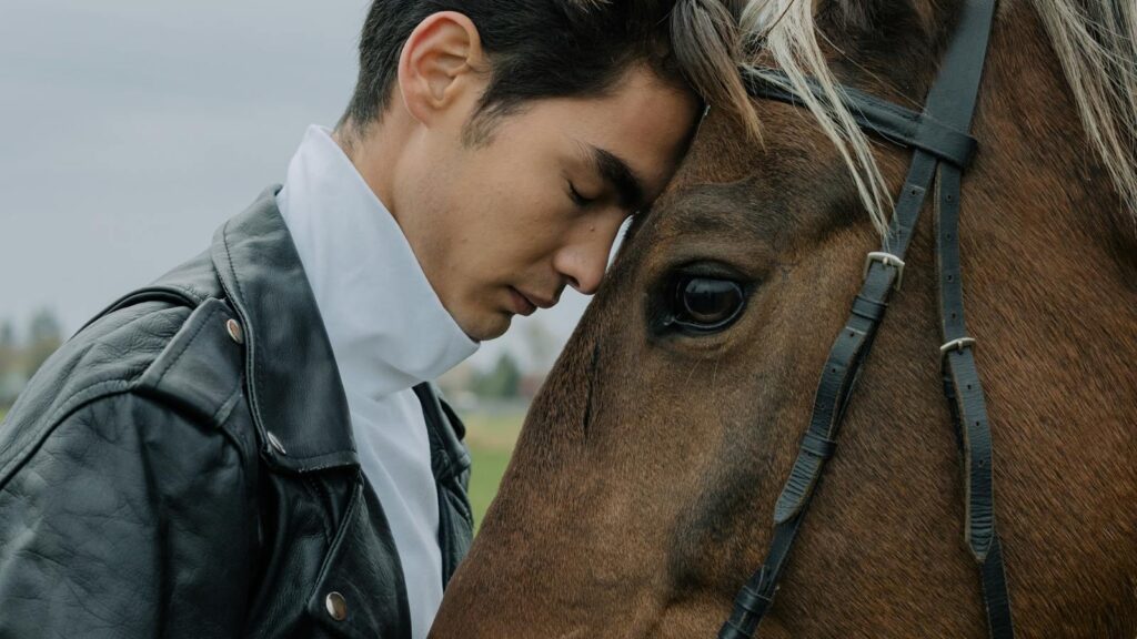 a man gently leaning against a horse outdoors.
