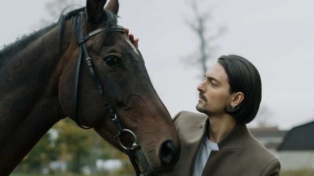 A man gently pats a horse in a serene outdoor setting, showcasing a bond between human and animal.