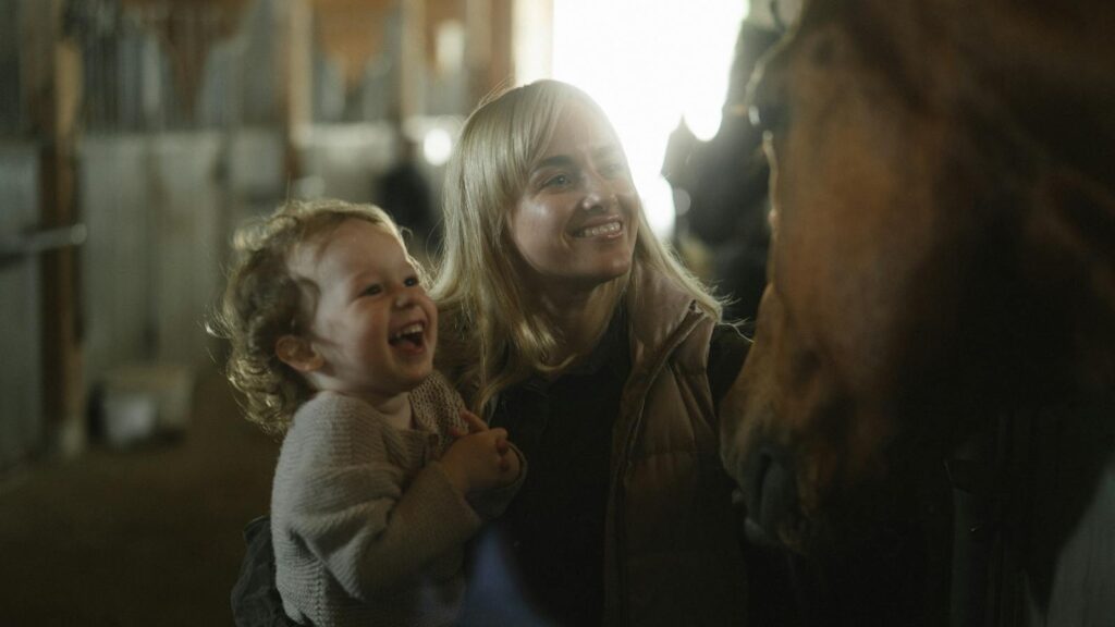 A joyful moment between mother and child interacting with a horse in a stable.