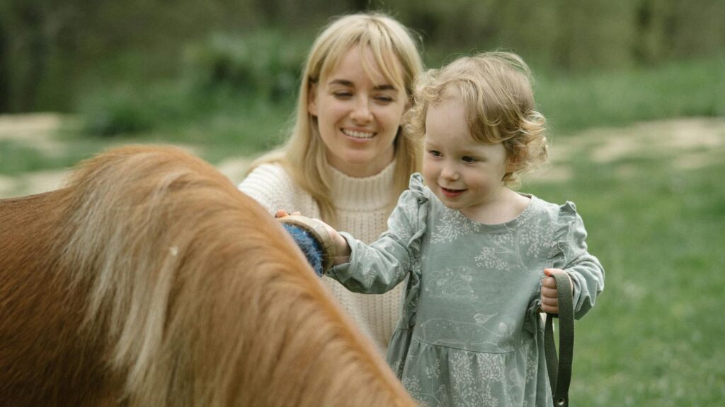 A joyful moment with a mother and daughter brushing a horse outdoors.