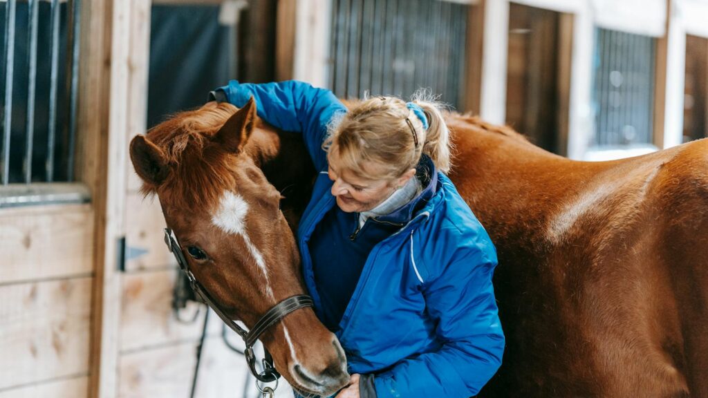 A woman lovingly embraces a horse in a rustic stable setting, showcasing equestrian care and bonding.