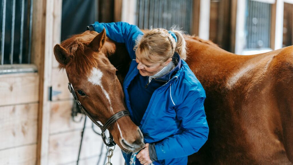 A woman lovingly embraces a horse in a rustic stable setting, showcasing equestrian care and bonding.