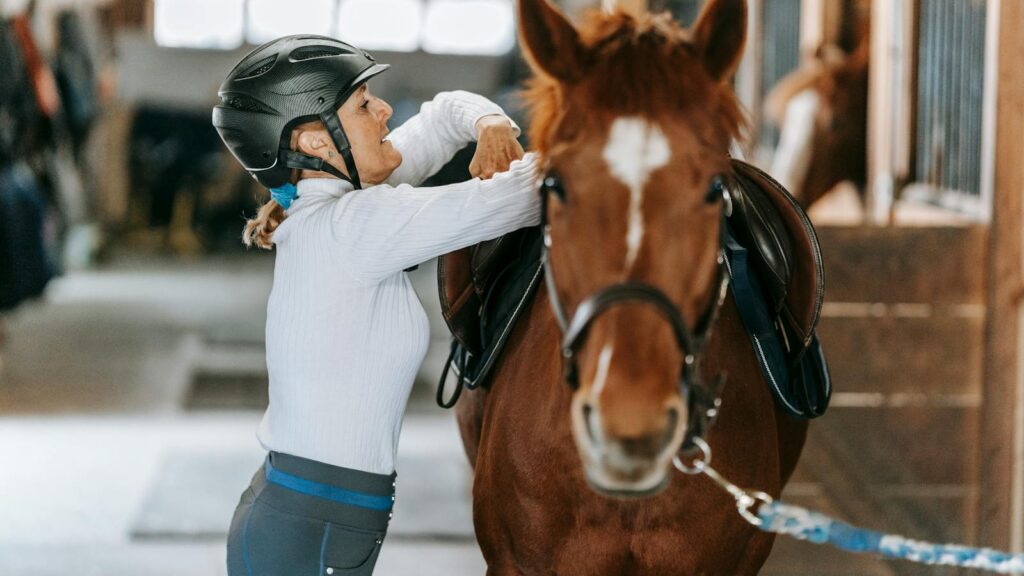 A woman prepares her horse in an indoor stable, showcasing equestrian skills.