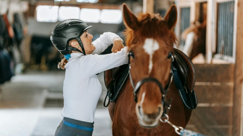 A woman prepares her horse in an indoor stable, showcasing equestrian skills.