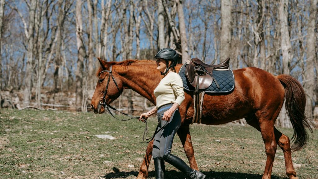 A woman guides her horse through a sunlit forest in spring, showcasing equestrian lifestyle.