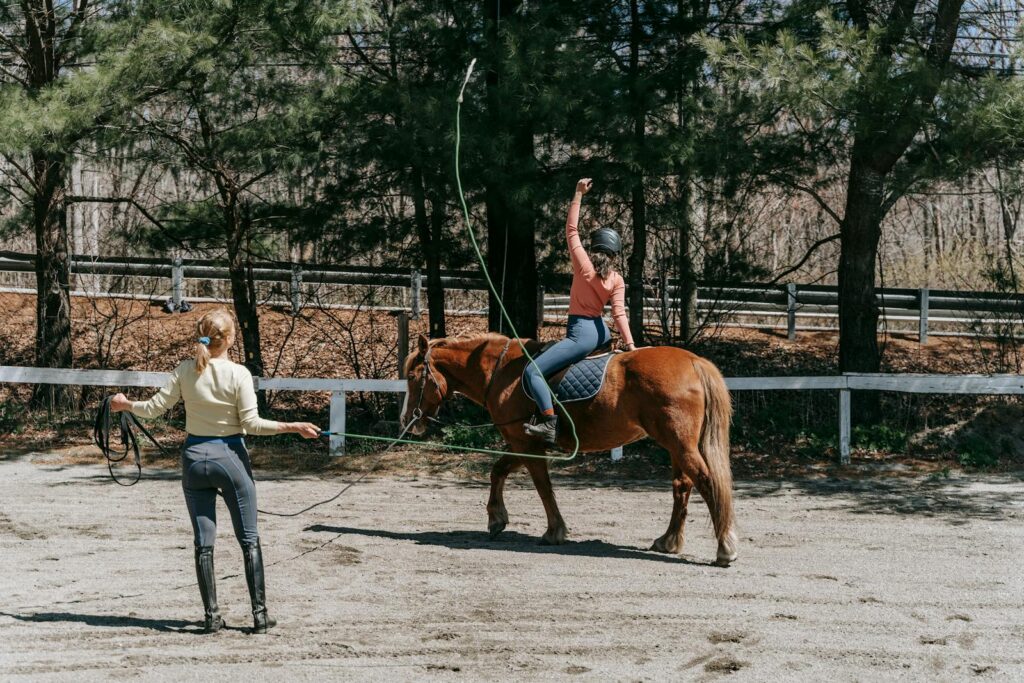 Two people engaged in horse riding training outdoors on a sunny day.