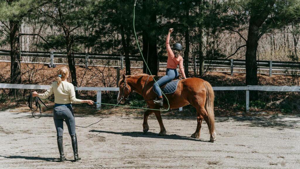 Two people engaged in horse riding training outdoors on a sunny day.