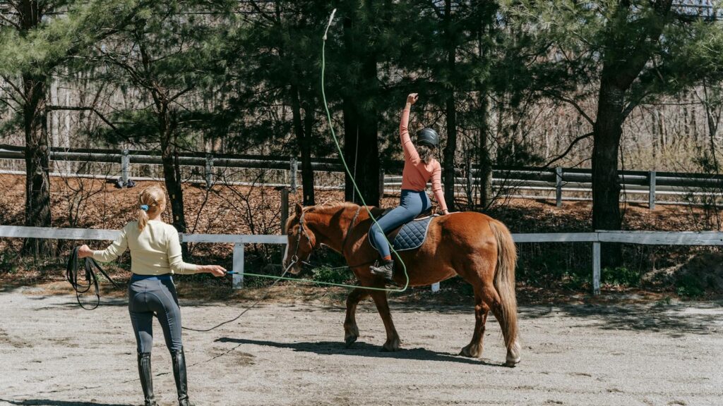 Two people engaged in horse riding training outdoors on a sunny day.