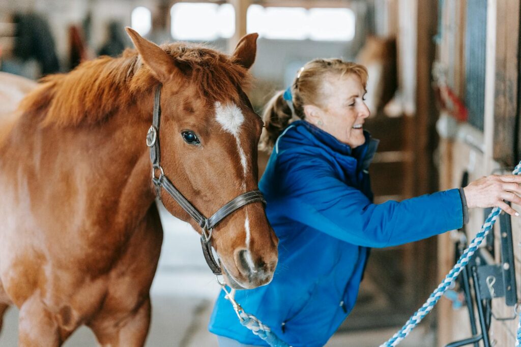 A woman interacts with a horse inside a stable, displaying care and affection.