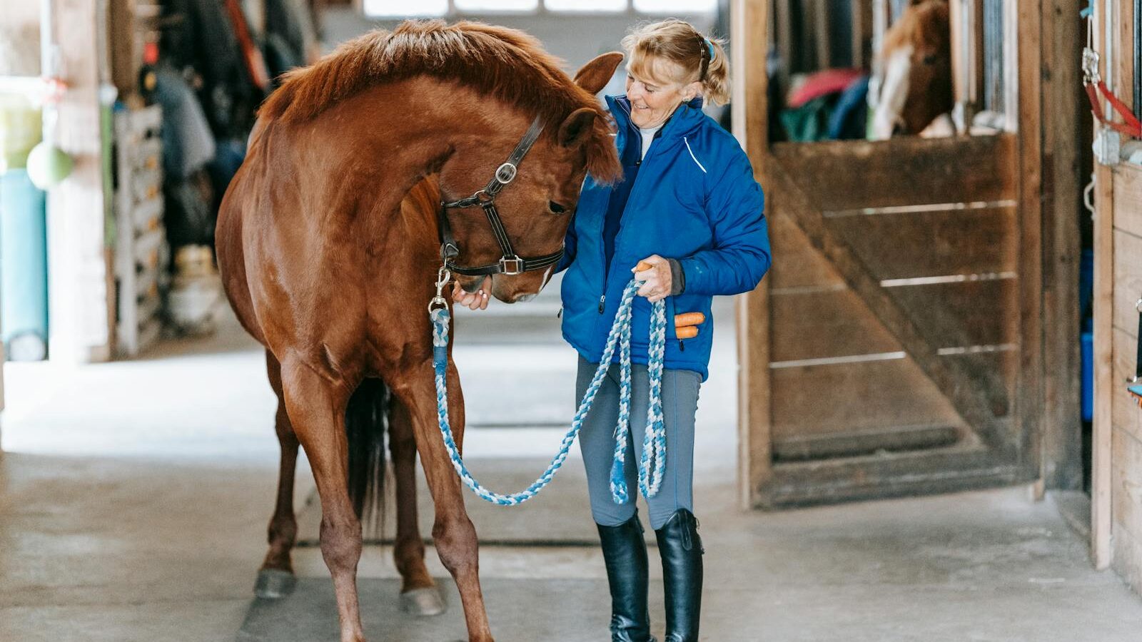 A woman showing affection to her horse inside a stable, demonstrating care and companionship.