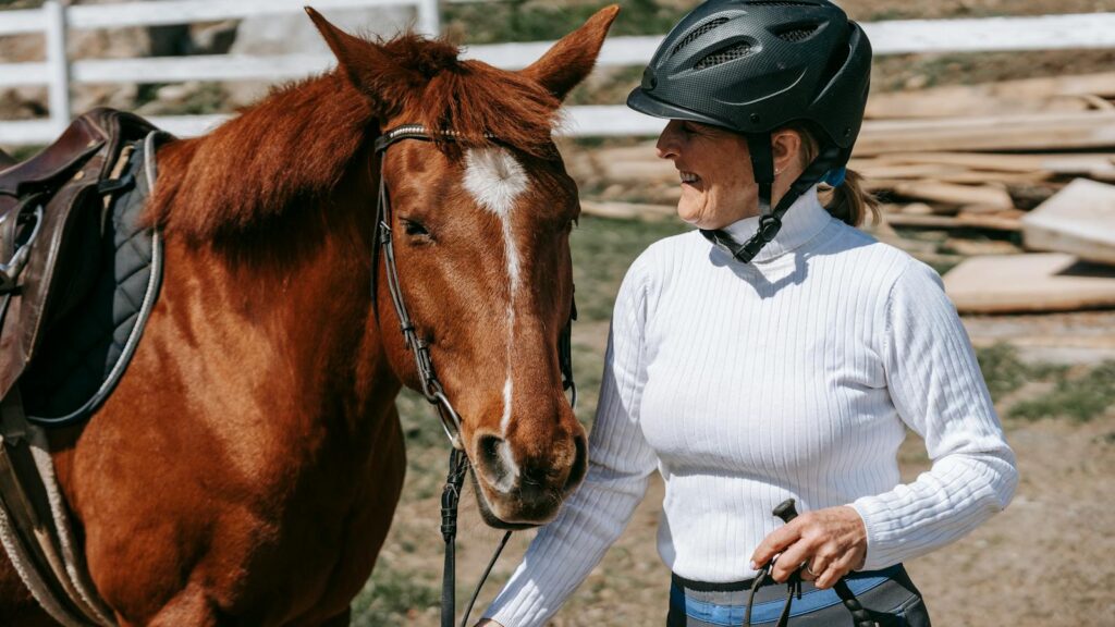 Smiling woman with helmet holding a horse outdoors on a sunny day.