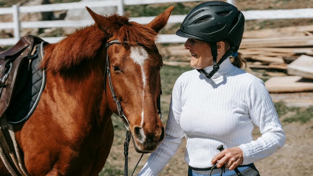 Smiling woman with helmet holding a horse outdoors on a sunny day.