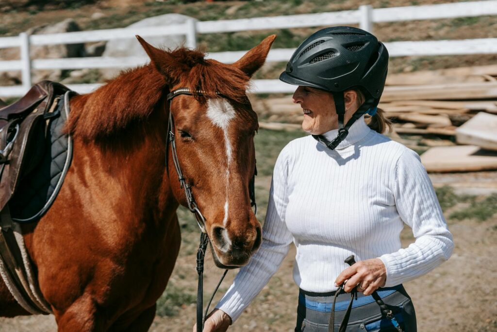 Smiling woman with helmet holding a horse outdoors on a sunny day.
