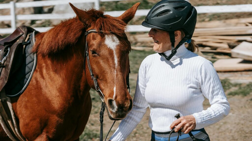 Smiling woman with helmet holding a horse outdoors on a sunny day.