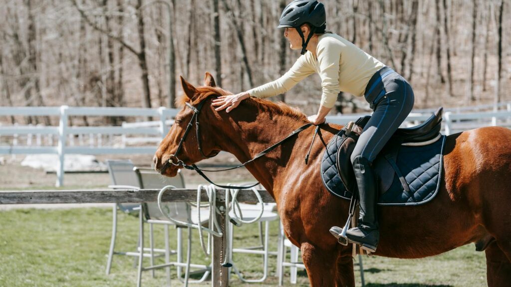 A woman in a helmet pats her horse while riding outdoors in a serene setting. Capturing camaraderie and leisure.