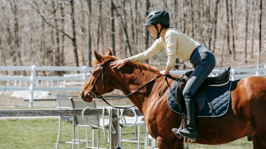 A woman in a helmet pats her horse while riding outdoors