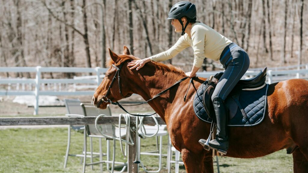 A woman in a helmet pats her horse while riding outdoors in a serene setting. Capturing camaraderie and leisure.