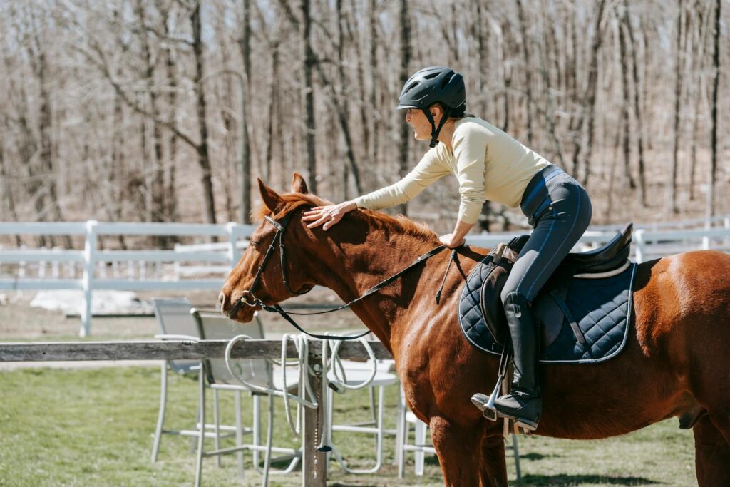 A woman in a helmet pats her horse while riding outdoors in a serene setting. Capturing camaraderie and leisure.