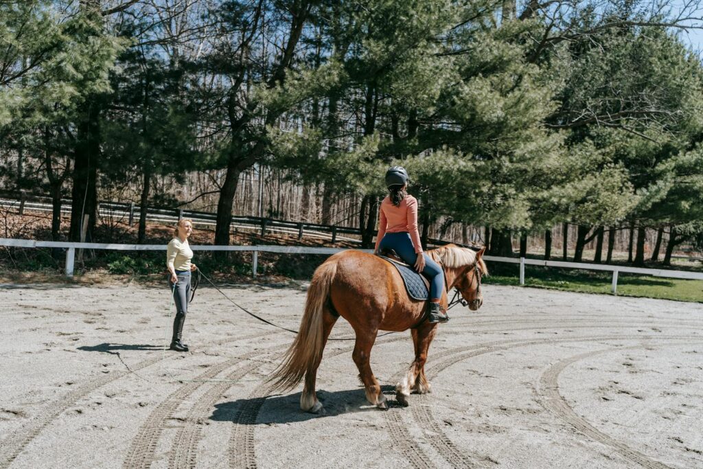 Woman on horseback receiving instruction in outdoor equestrian setting.