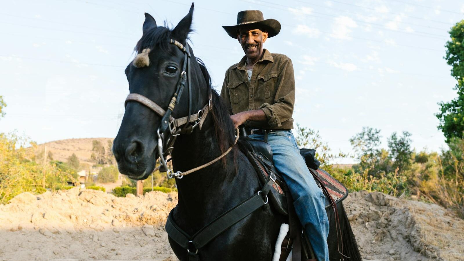A smiling cowboy rides his horse outdoors, capturing the essence of rural life.