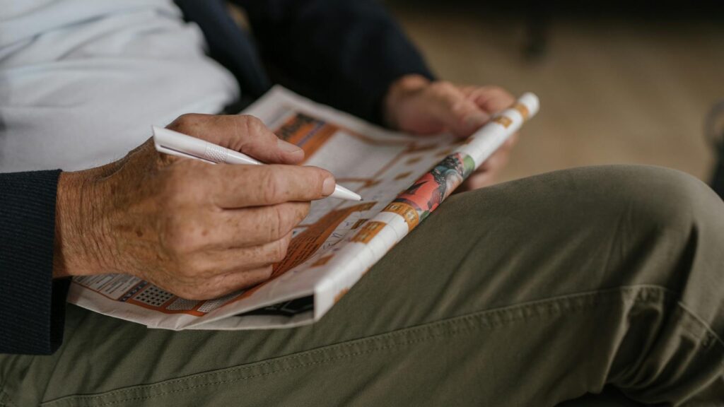 Close-up of a senior adult solving a crossword puzzle in a newspaper with a pen.
