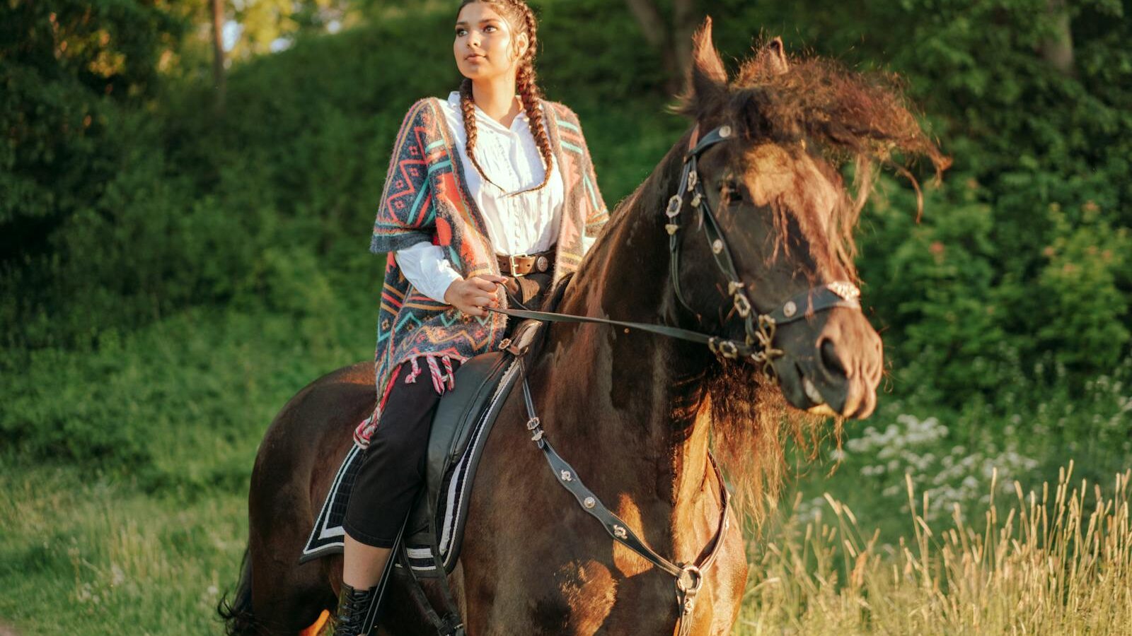 A woman enjoys a serene horseback ride through a lush green landscape at sunset.
