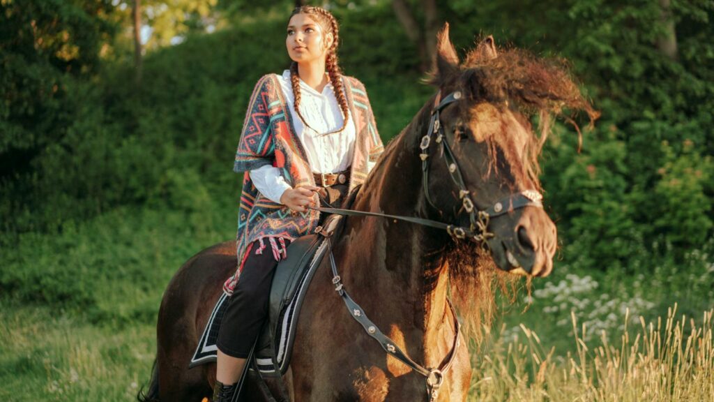 A woman enjoys a serene horseback ride through a lush green landscape at sunset.