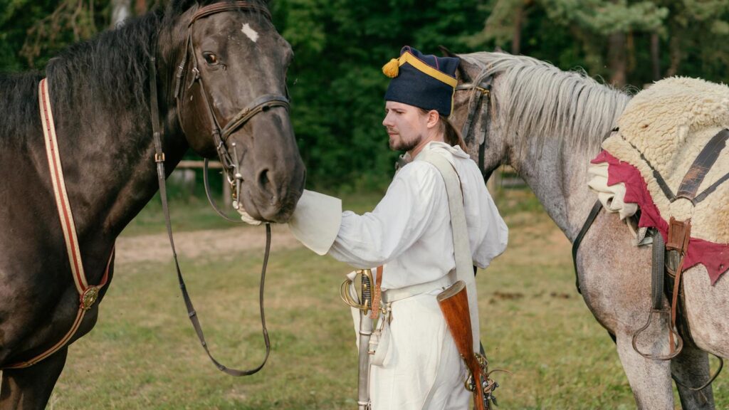Man in historical military uniform with horses in a reenactment setting outdoors.