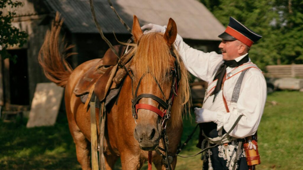 A man in a military uniform stands with a saddled horse outdoors.