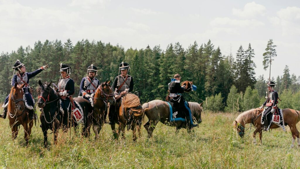 Group of soldiers on horseback in historical military uniforms during a reenactment outdoors.