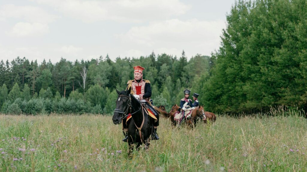 Group of cavalry riders in historic uniforms in a lush meadow setting.