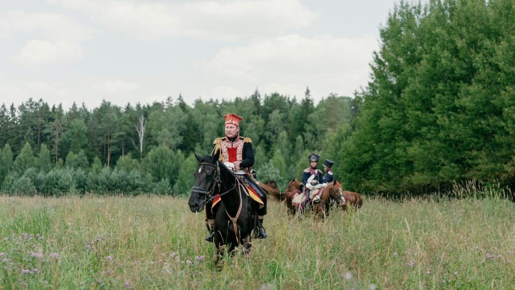 Group of cavalry riders in historic uniforms in a lush meadow setting.