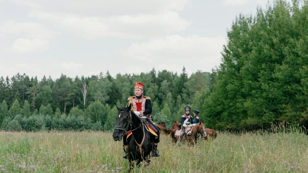 Group of cavalry riders in historic uniforms in a lush meadow setting.